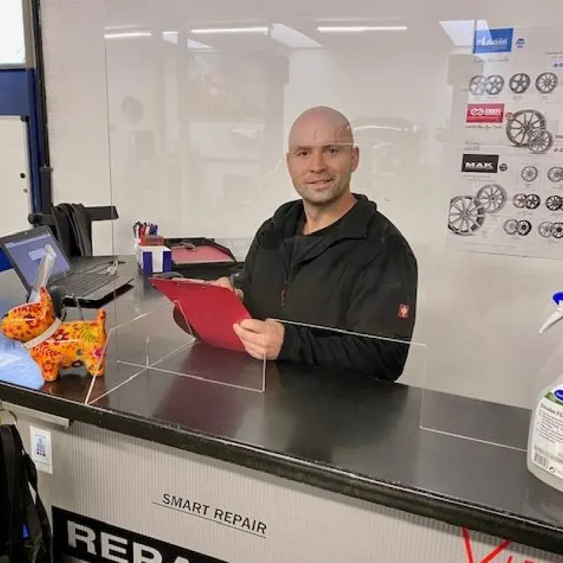 Mitarbeiter am Annahmetresen der Werkstatt, im Hintergrund eine Felgenübersicht