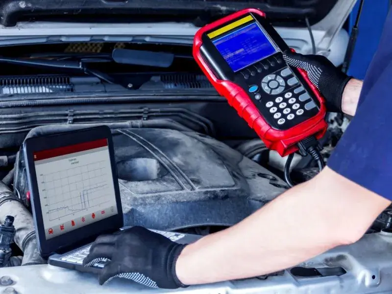 Techniker prüft mit einem Diagnosegerät die Elektrik im geöffneten Motorraum